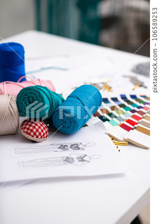 Macrame threads coils and needle cushion on tailor table in fashion studio colorful yarn sketch and swatch for dress craft in sewing workshop seamstress supplies closeup 106589253
