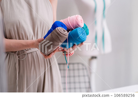 Fashion designer holds pile of macrame yarn coils in fashion studio woman dressmaker shows threads bobbins for macrame craft in sewing workshop closeup 106589256
