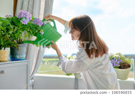 Woman watering potted plants from watering can on outdoor terrace at home 106590855