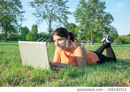 Young Caucasian woman lying on park using her laptop very happy Young Caucasian woman lying on park using her laptop very happy 106592012