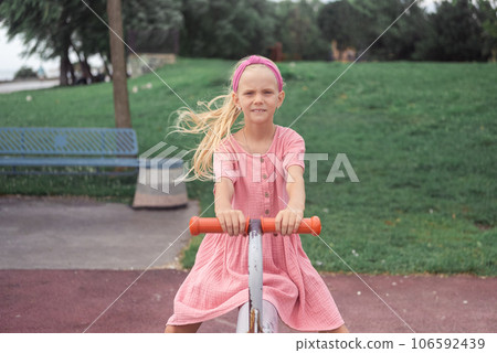 A child, joyfully riding a seesaw in the urban park's playground, shares smiles and laughter while having a blast. A child, joyfully riding a seesaw in the urban park's playground, shares smiles and laughter while having a blast. 106592439