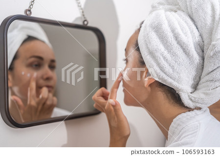 Home beauty ritual: A woman's reflection in the mirror as she diligently applies moisturizer, elevating her daily skincare. Home beauty ritual: A woman's reflection in the mirror as she diligently applies moisturizer, elevating her daily skincare. 106593163