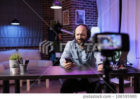 Content creator doing live broadcasting for online streaming service reading comments from audience. Internet streamer interacting with fans while recording in home studio Content creator doing live broadcasting for online streaming service reading comments from audience. Internet streamer interacting with fans while recording in home studio 106595980