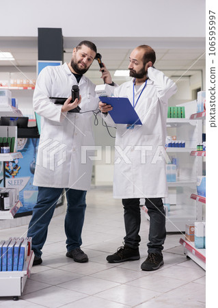 Drugstore workers looking at pills packages checking medical label during pharmacy inventory, looking at clipboard full with drugs information. Pharmacists is responsible for organizing medication 106595997