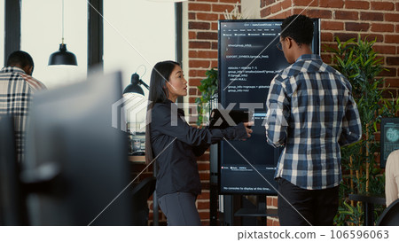 Team of coders analyzing code on wall screen tv comparing errors using digital tablet next to programer working with neural network. Software engineers collaborating on coding group project. 106596063