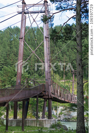 A wooden bridge with metal supports across a raging river in the Altai Mountains. Old broken bridge A wooden bridge with metal supports across a raging river in the Altai Mountains. Old broken bridge 106597729