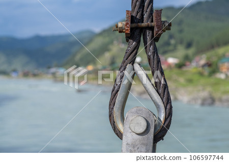 Reliable strong metal cable with connecting fastening with bolts and nuts of different sizes, outdoors. metal loop with steel wire as part of a bridge 106597744