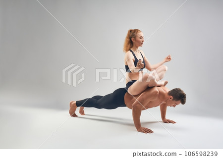 Strong man doing push ups with partner in lotus pose on white background 106598239