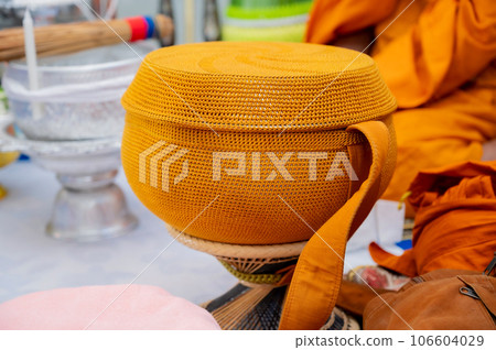 A metal alms bowl covered with golden-orange cloth to receive food from laypeople and people who believe in Buddhism. A metal alms bowl covered with golden-orange cloth to receive food from laypeople and people who believe in Buddhism. 106604029