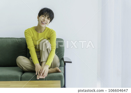 Fashion portrait of a young woman in yellow clothes sitting on a green sofa against white background Fashion portrait of a young woman in yellow clothes sitting on a green sofa against white background 106604647