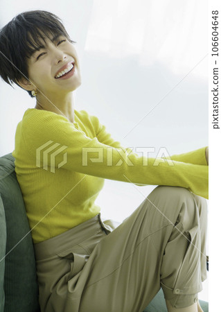 Fashion portrait of a young woman wearing yellow clothes sitting on a green sofa against a white background, vertical position Fashion portrait of a young woman wearing yellow clothes sitting on a green sofa against a white background, vertical position 106604648