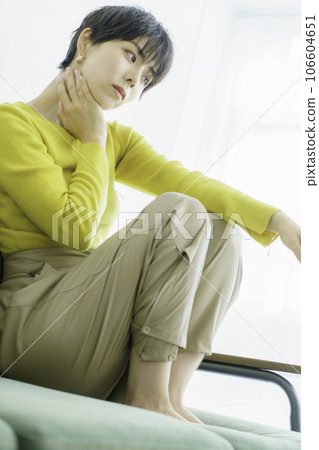 一位身穿黃色衣服的年輕女子坐在白色背景的綠色沙發上，垂直位置 106604651