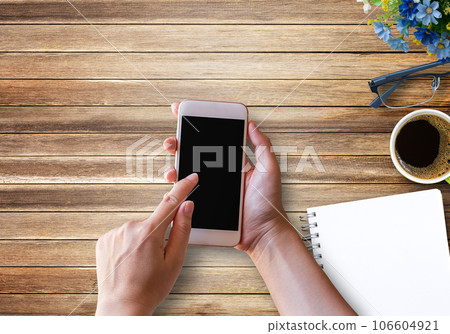 Hand holding smartphone with blank notebook coffee cup and glasses on wood background. Hand holding smartphone with blank notebook coffee cup and glasses on wood background. 106604921