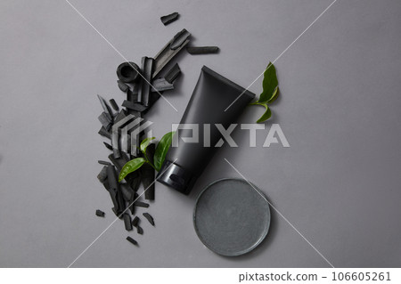 Glass petri dish of clay mask texture displayed with black tube with activated bamboo charcoal and green tea leaves. Activated bamboo charcoal is applied in many different areas of life 106605261