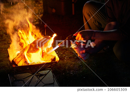 A man's hands apply a gas torch to firewood placed in a bonfire stand to increase the firepower. A man's hands apply a gas torch to firewood placed in a bonfire stand to increase the firepower. 106605309