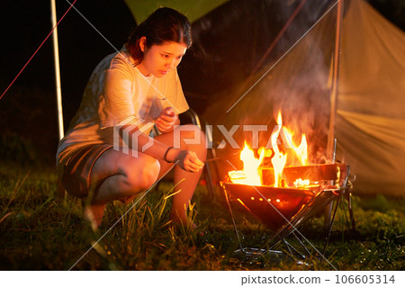 Young woman enjoying a bonfire near a tent Young woman enjoying a bonfire near a tent 106605314