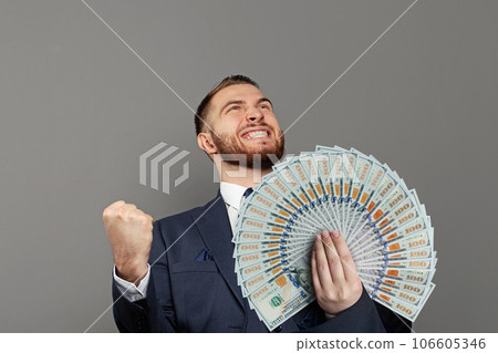 Excited businessman in suit with us dollars banknotes fan in hand against grey background. Excited businessman in suit with us dollars banknotes fan in hand against grey background. 106605346