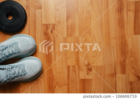 New light blue green female running shoes and weight plate on emty wooden floor. Stylish monochrome shoes for active people that incorporate new health technology. Top view 106606719