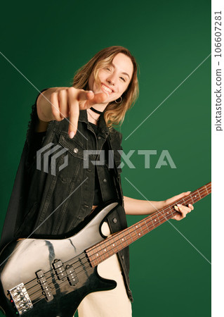 Portrait of young girl, musician in stylish clothes, making performance, playing electric guitar against green studio background Portrait of young girl, musician in stylish clothes, making performance, playing electric guitar against green studio background 106607281
