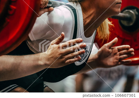 female powerlifter during squat powerlifting, coach hands are on safety net female powerlifter during squat powerlifting, coach hands are on safety net 106607301