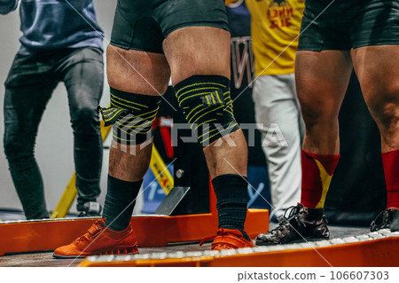 male powerlifter preparing for squat powerlifting, knees are wrapped with an elastic bandage male powerlifter preparing for squat powerlifting, knees are wrapped with an elastic bandage 106607303