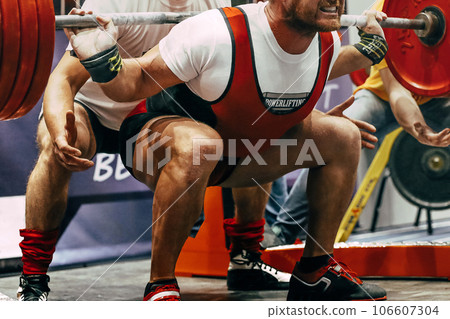 close-up male powerlift squat in powerlifting, coach hands are on safety net close-up male powerlift squat in powerlifting, coach hands are on safety net 106607304