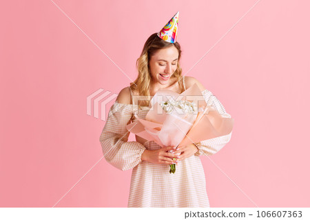Tender, attractive young girl in cute dress standing with flowers bouquet against pink studio background. Birthday Tender, attractive young girl in cute dress standing with flowers bouquet against pink studio background. Birthday 106607363