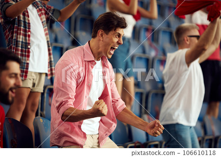 Winning game. Young people, football fans cheering up favourite team during live match on stadium. Expressing emotions Winning game. Young people, football fans cheering up favourite team during live match on stadium. Expressing emotions 106610118