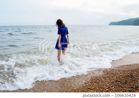 Upset thoughtful woman in blue dress going to the sea in cloudy weather before rain. She looking into the water Upset thoughtful woman in blue dress going to the sea in cloudy weather before rain. She looking into the water 106610429