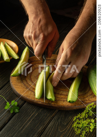 Delicious salad for lunch with fresh cucumber and parsley. Chef hands with knife slicing cucumbers on kitchen cutting board Delicious salad for lunch with fresh cucumber and parsley. Chef hands with knife slicing cucumbers on kitchen cutting board 106610928