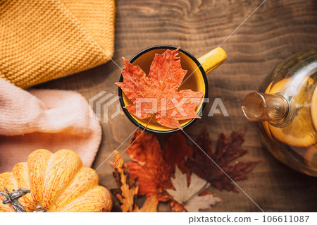 Brewed herbal tea with lemon in a glass teapot next to a pumpkin on a wooden table with maple leaves 106611087