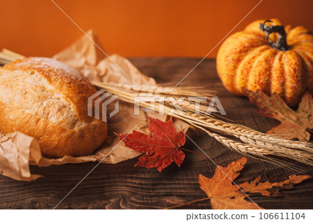 Fresh loaf of bread with ears of wheat and pumpkin on a wooden background 106611104