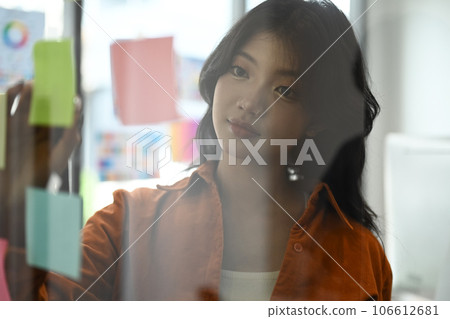 Charming young startup businesswoman reading notes on transparent board, planning goals, manage corporate work tasks Charming young startup businesswoman reading notes on transparent board, planning goals, manage corporate work tasks 106612681