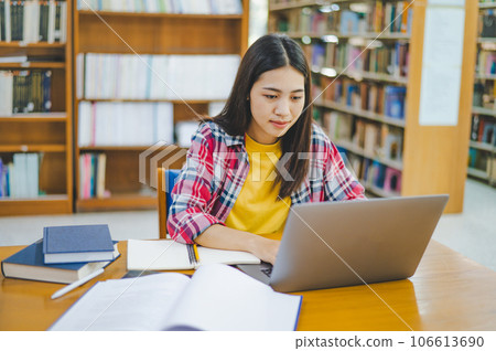 Female college student working on laptop and searching for books to study, make report, find useful information in college room. Concept of reading, learning and intelligence. 106613690