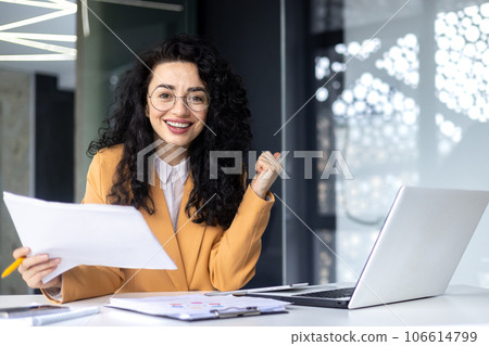 Portrait of a successful woman winner behind a paper work, businesswoman smiling and looking at the camera, financier holding a successful report of the company in hands, satisfied with achievement. Portrait of a successful woman winner behind a paper work, businesswoman smiling and looking at the camera, financier holding a successful report of the company in hands, satisfied with achievement. 106614799