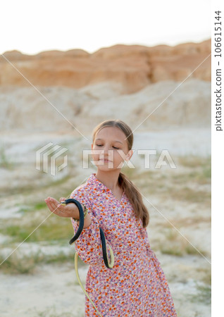 A teenage girl plays with a snake, holding it in her hands. Children and snake in the wild A teenage girl plays with a snake, holding it in her hands. Children and snake in the wild 106615144