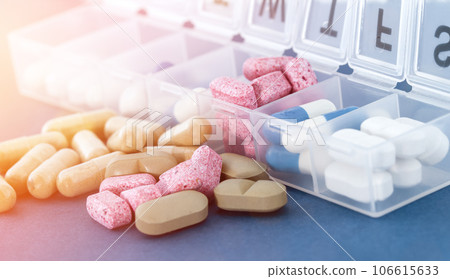 Weekly pill organizer or daily medicine pill box on blue background in bright sun rays. 106615633