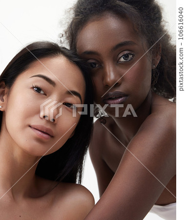 Portrait of beautiful young african and asian women with well-kept skin looking at camera against white background 106616040