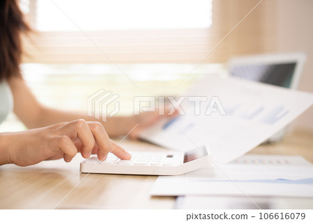 Asian woman working at home, Press the calculator to calculate the income - expenses of the house and use the laptop to record the information and check the accuracy, Home lifestyle. Asian woman working at home, Press the calculator to calculate the income - expenses of the house and use the laptop to record the information and check the accuracy, Home lifestyle. 106616079