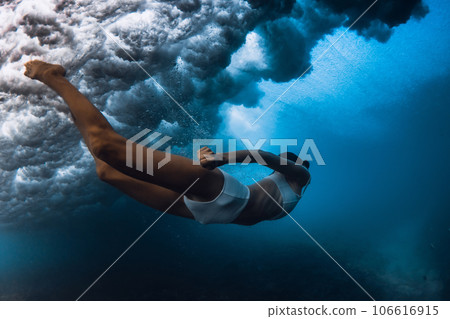 Woman dive under wave. Duck dive under crashing barrel wave in transparent ocean Woman dive under wave. Duck dive under crashing barrel wave in transparent ocean 106616915