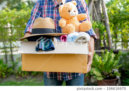 Volunteer woman provide clothing donation box with used clothes and doll to support help for refugee, homeless or poor people in the world. Volunteer woman provide clothing donation box with used clothes and doll to support help for refugee, homeless or poor people in the world. 106616970