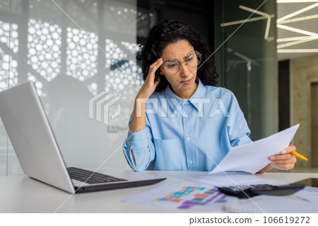 Upset and disappointed woman behind paperwork, hispanic woman reading and checking financial report, financial accountant behind paperwork with contracts and bills. 106619272