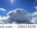 large white cloud against a bright blue sky. The cumulus nature of the clouds is a harbinger of a downpour 106619490