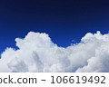 large white cloud against a bright blue sky. The cumulus nature of the clouds is a harbinger of a downpour 106619492