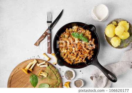 Cooked chanterelle mushrooms with onions and spices in a pan on the kitchen table grnished with potatoes. top view 106620177