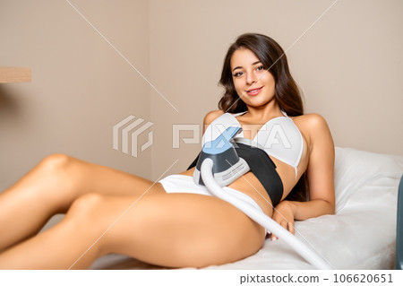 A young and joyful brunette reclines on a beauty salons couch, undergoing a body sculpting procedure with a radiant smile.  106620651