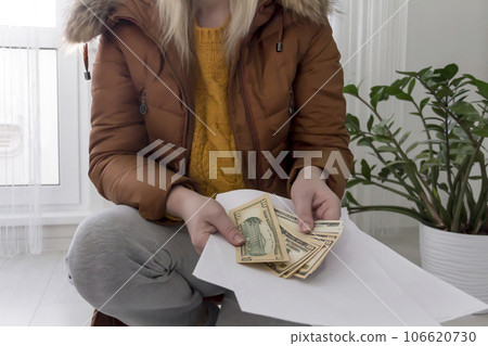 A woman warmly dressed in a brown jacket and hat is sitting near a heating appliance with bills A woman warmly dressed in a brown jacket and hat is sitting near a heating appliance with bills 106620730