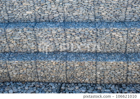 A stone dam made of small stones, strengthening the shore with rubble, screed stones with rabitz mesh, flood protection, a breaking rampart, a pile of stones. 106621010