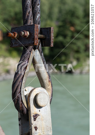 Reliable strong metal cable with connecting fastening with bolts and nuts of different sizes, outdoors. metal loop with steel wire as part of a bridge Reliable strong metal cable with connecting fastening with bolts and nuts of different sizes, outdoors. metal loop with steel wire as part of a bridge 106621057