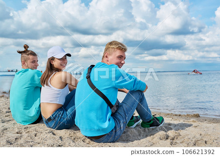 Back view of three teenage friends sitting at beach, looking at sea 106621392